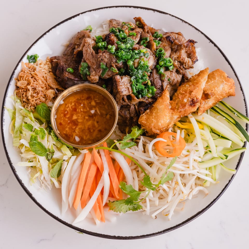 A large bowl of Lantern House Kitchen & Bar's Asian-fusion dish with grilled meat, spring rolls, and fresh vegetables.