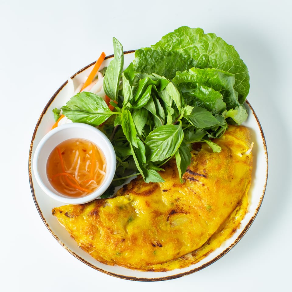 A golden-yellow Lantern House Kitchen & Bar savory crepe with fresh herbs, pickled vegetables, and dipping sauce.