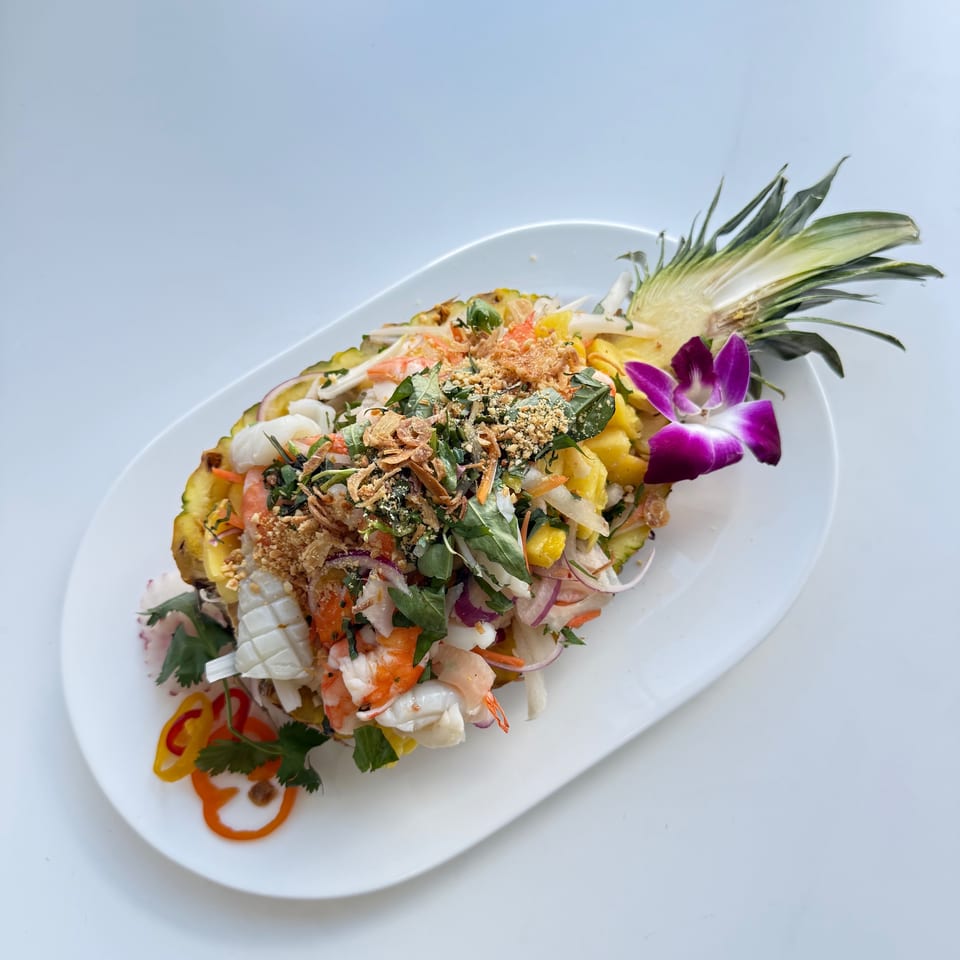 Asian-fusion seafood salad with shrimp, squid, and herbs, served in a pineapple half with an orchid.