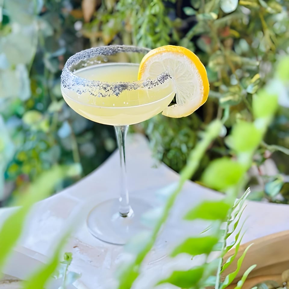 A Lantern House Kitchen & Bar cocktail, garnished with a lemon slice and a salted rim, against a leafy green background.